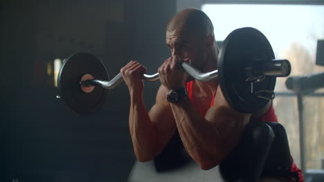 male-athlete-lifts-a-barbell-with-weight-sitting-on-a-bench.-Slow-motion-exercise-of-the-hands.